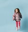 Little girl dressed in pink faux fur coat, pants and boots. She smiling, gesticulating, posing on blue background. Full length