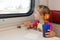 Little girl drinking tea with a sandwich on train at the table on outboard second-class carriage and enthusiastically looking