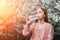 A little girl drinks clean fresh water from a plastic bottle near a flowering tree in the garden