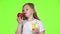 Little girl drinks juice from a glass and holds an apple. Green screen. Slow motion