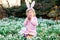 Little girl with Easter bunny ears making egg hunt in spring forest on sunny day, outdoors. Cute happy child with lots