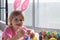 Little girl in Easter bunny ears painting colored eggs