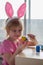Little girl in Easter bunny ears painting colored eggs