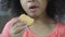 Little girl eating tasty cookie with appetite, unhealthy food, close-up
