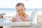 A little girl eats a delicious banana on a tropical sandy beach. Looking down. The baby meets with food. The development of fine