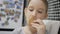 Little girl eats gingerbread cookies sitting in kitchen. Winter holidays.