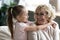 Little girl embracing shoulders of smiling sincere older senior granny.