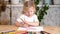 A little girl enthusiastically draws a heart with colored pencils sitting at the table at home alone