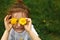 A little girl of European appearance with light hair puts yellow dandelion flowers to her eyes and enjoys the summer,