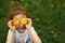 A little girl of European appearance with light hair puts yellow dandelion flowers to her eyes and enjoys the summer,