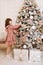 Little girl in a festive outfit is decorating Christmas tree with garlands, glass balls and Christmas toys. Gift boxes
