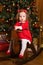 Little girl in a festive red dress on a wooden swing rocking horse. Christmas parties are a fabulous time for children