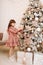 Little girl in festive soft pink dress is decorating Christmas tree with garlands, glass balls and Christmas toys. Gift