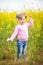 A little girl in a field of rapeseed with a bunch of chamomiles