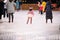 Little girl figure skater in a pink sweater rides on winter evening on an outdoor ice rink among adults, rear view