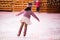 Little girl figure skater in pink sweater is skating on winter evening at an outdoor ice rink, back view