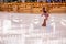 Little girl figure skater in pink sweater is skating on winter evening on an outdoor ice rink lit by garlands