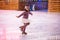 Little girl figure skater in a pink sweater is skating on winter evening on an outdoor ice rink lit by garlands