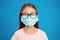 Little girl with foggy glasses caused by wearing disposable mask on blue background. Protective measure during coronavirus