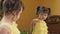 The little girl in front of the mirror bites her lip. A beautiful child in a yellow dress by the mirror. Girl with tails.