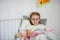 Little girl in glasses reading a book while lying in bed.