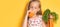 Little girl in a gown with floral patteern drinking carrot juice holding bunch of carrots in hand. Waist up shot