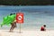 Little girl with a green crocodile-shaped boat passes behind a red bathing sign