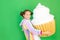 A little girl on a green isolated background in a bright suit holds a huge cake. Space for text. Concept of junk food and weight