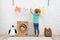 Little girl hanging clean laundry near toy cardboard washing machine indoors