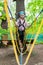 Little girl in harness crossing rope bridge in a ropes course