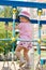Little girl in hat climbs on children playground at sunny d