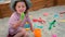 Little girl in hat and dress plays with toys in sand pit