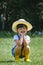 Little girl in a hat makes cute poses and smiles at the camera sitting in the grass on a bright summer day. Cute girl playing in a