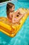Little girl in hat relaxing in swimming pool, swims on inflatable yellow mattress