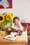 The little girl is having breakfast at home. On the table is a bouquet of flowers of sunflowers and a sweet pie with fruit,
