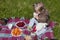 Little girl having a picnic on a green lawn. Purple blanket with plates of berries and fruits, teddy bear and a toy sheep.