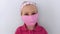 Little girl in headband wearing protective pink fabric mask against coronavirus COVID-19 pandemic white background.Wuhan virus epi