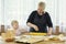 A little girl helps her grandmother roll out the pizza dough.