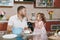 Little girl helps man to cook Christmas ginger cookies feeding daddy in kitchen at table. Happy family dad, child