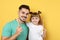 Little girl and her father with toothbrushes on color background