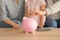 Little girl with her parents  putting coins into piggy bank indoors. Money savings concept