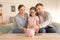 Little girl with her parents  putting coins piggy into bank indoors. Money savings concept