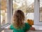 A little girl with her teddy bear looks out the window at the garden.