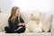 Little girl with her white teddy bear having conversation on the sofa.