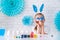 The little girl hides her eyes behind them with blue Easter eggs. A child with bunny ears is enjoying Easter. Home decoration in