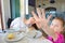 little girl hiding with hand eating in restaurant with her mother