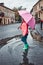 Little girl holding big pink umbrella walking in a downtown on rainy gloomy autumn day