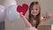 Little girl holding big red paper heart and zero waste gift on background of air balloons. Valentines Day, love, mothers