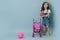 Little girl holding a doll next to a pram and pink gymnastic ball over blue