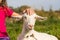 Little Girl Holding Leash And Stroking Goat On Meadow